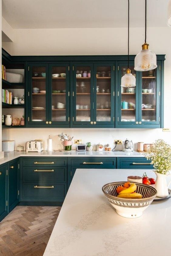 a chic and refined teal kitchen with glass and usual cabinets, white countertops and a white backsplash plus pendant lamps