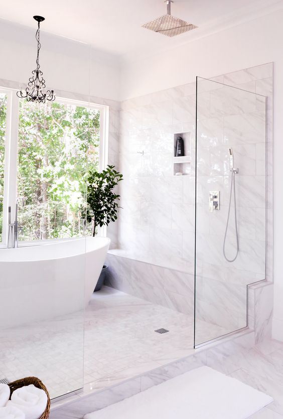a refined modern bathroom clad with white marble, with a glass shower and a large window for the view