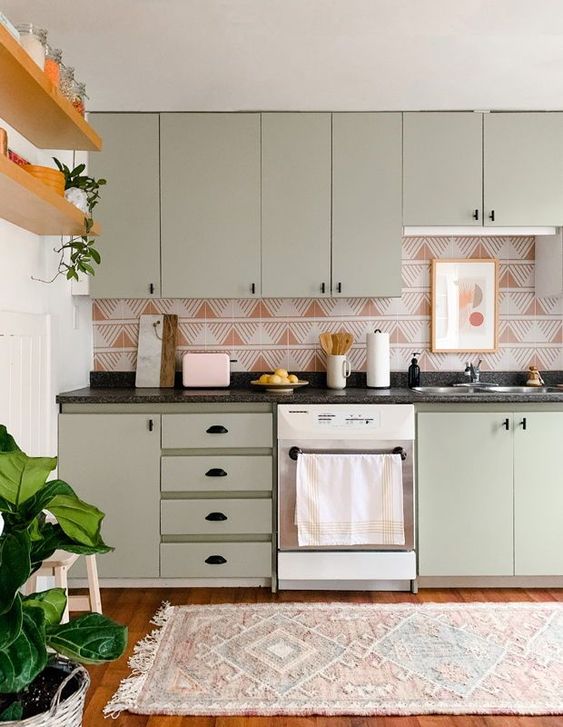 An olive green kitchen with black handles and a very eye catchy rust and white geometric print backsplash that stands out