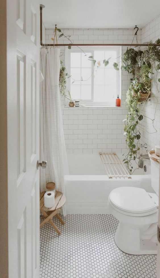 a small boho bathroom in white, with subway tiles, marble penny tiles and potted greenery to refresh the space