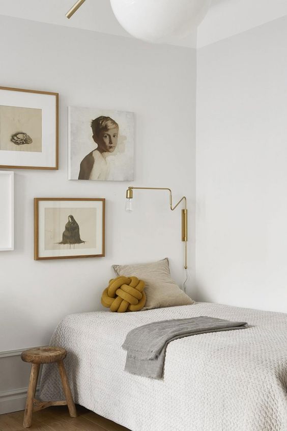 a Japandi guest bedroom in neutrals, with a gallery wall, a bed and a stool, a gold sconce and pretty pillows