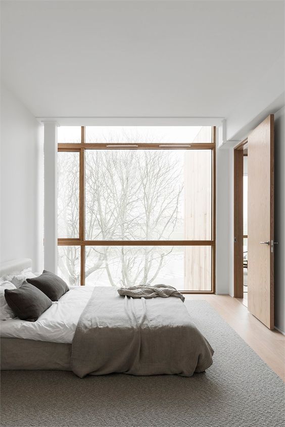 a minimalist Japandi bedroom in white and grey, with a glazed wall for a lovely view and light stained wooden floors