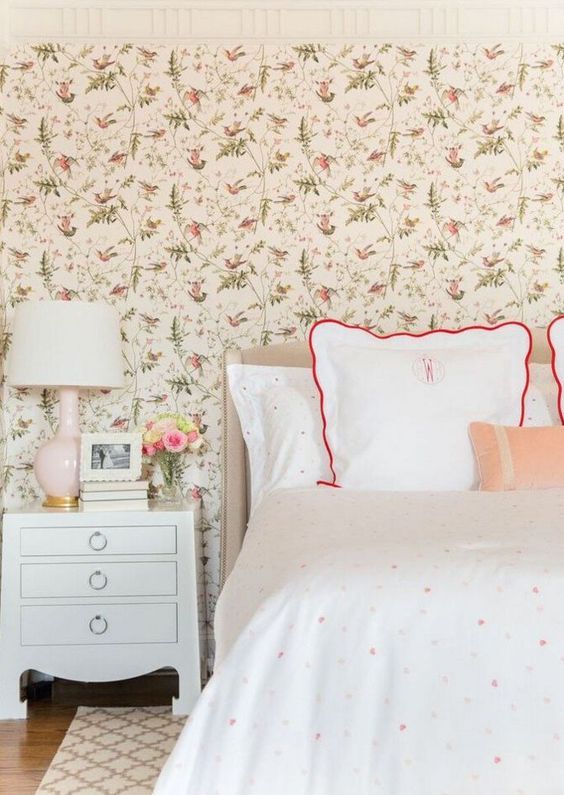 A cozy vintage inspired bedroom with a floral wallpaper wall, polka dot bedding, vintage inspired furniture and a blush lamp