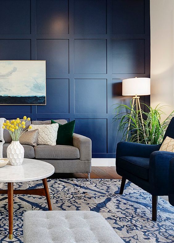 a modern living room with a navy panel wall, navy and grey furniture, potted greenery and a sea artwork