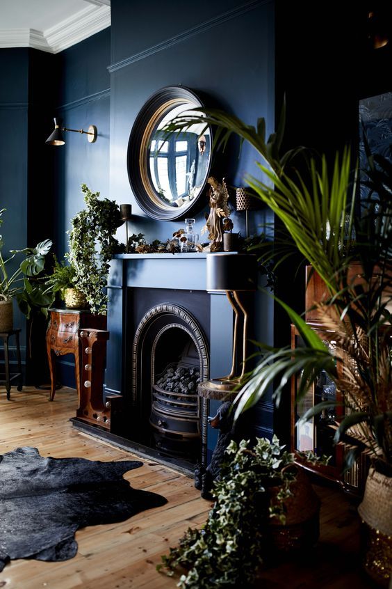 a moody refined living room in navy, with a fireplace, a mirror and heavy wooden furniture plus lots of plant