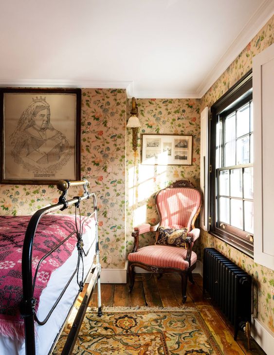 37 a vintage bedroom with floral wallpaper, a black forged bed, a vintage pink chair and printed textiles