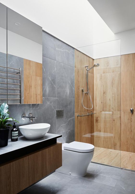 39 a contemporary bathroom with grey marble tiles and wooden paneling in the shower space, a floating vanity and a skylight