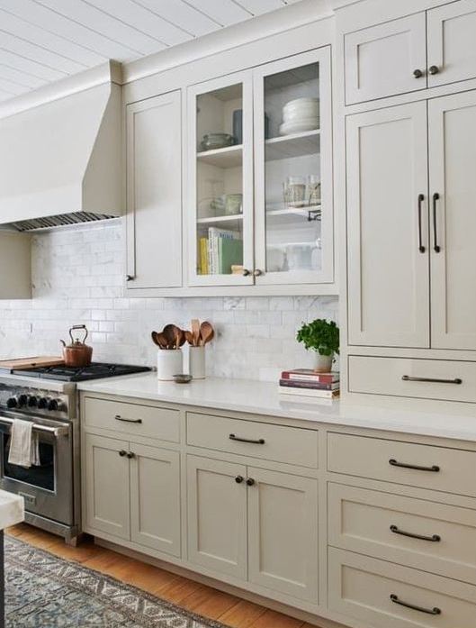 a contemporary greige kitchen with vintage cabinets, black handles and a white marble tile backsplash plus white countertops