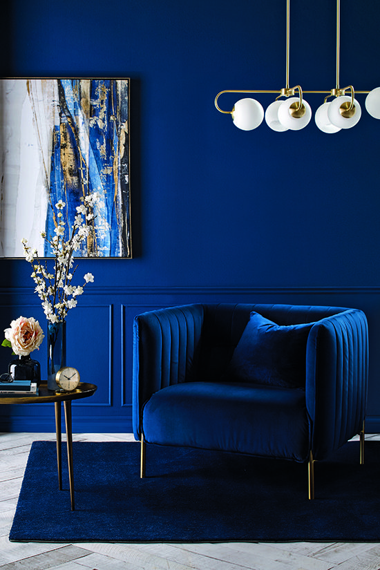 a bright living room with bold paneled walls, a bold blue chair, a modern chandelier and a gorgeous artwork