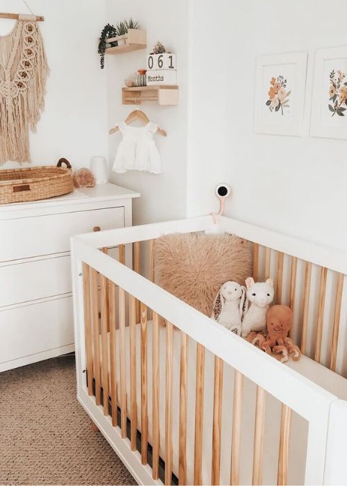 a neutral and earthy tone nursery with a macrame hanging, modern furniture, a gallery wall and pretty toys