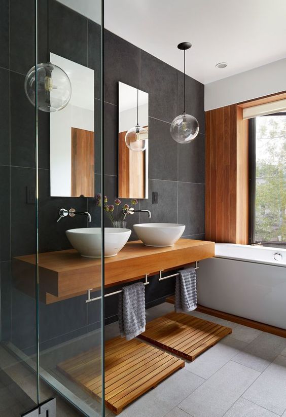 a contemporary bathroom with large scale dark grey tiles, a wooden accent wall, a floating vanity and mats
