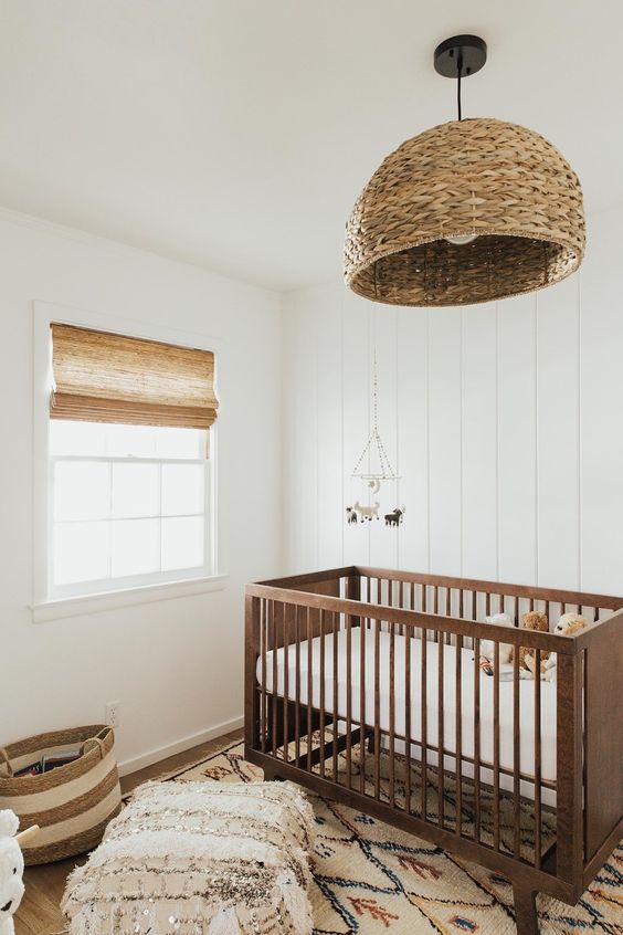 a neutral rustic nursery done with earthy tones and a rattan lamp, a stained crib and printed textiles