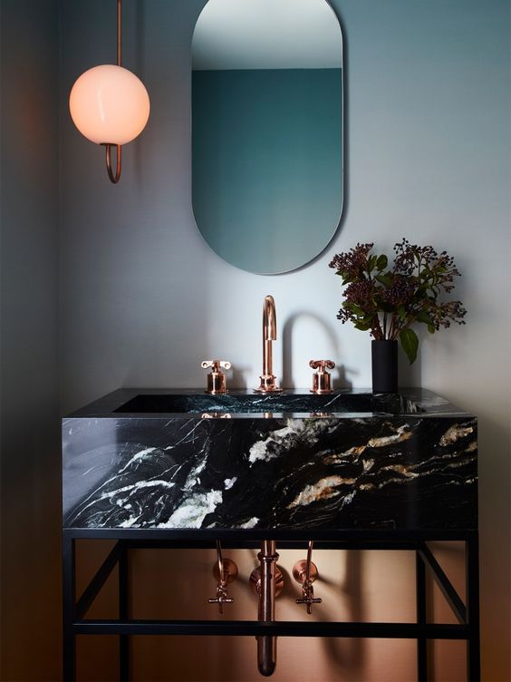 a catchy and refined bathroom in blue and orange, with a black marble vanity and copper fixtures is chic