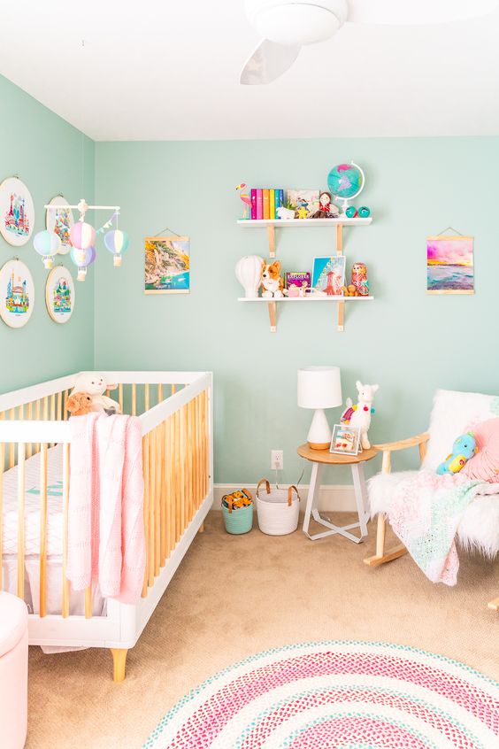 a pastel travel-themed nursery with turquoise walls, pink and mint touches and bright artworks