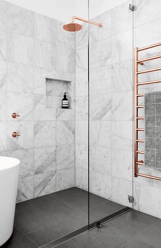 a chic bathroom with white marble tiles and a grey tile floor, copper fixtures for a softer and more refined touch