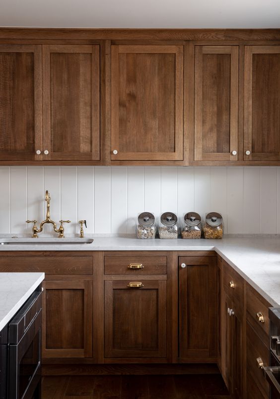 43 a classic walnut kitchen with vintage cabinetry, gold fixtures, a white tile backsplash and white stone countertops