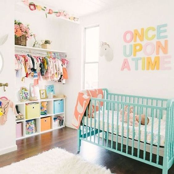 a neutral nursery with a turquoise crib and a pretty pastel letter artwork plus colorful clothes and boxes