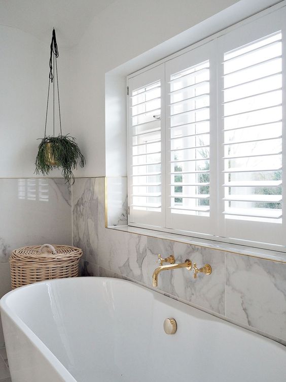 a chic and refined bathroom with grey marble tiles, a chic tub and gold fixtures plus potted greenery