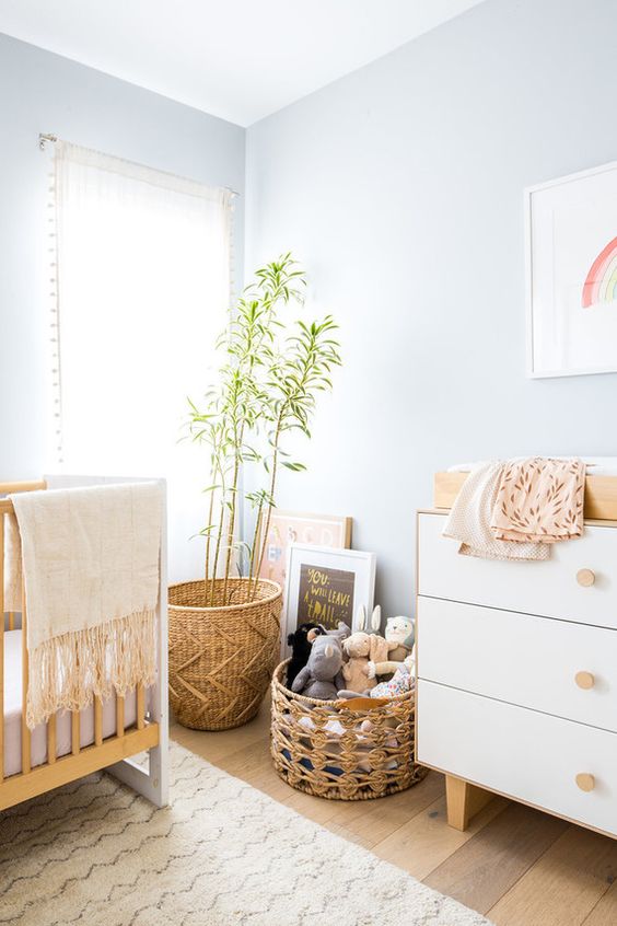 a pastel blue nursery with neutral furniture, baskets and potted greenery plus bright artworks