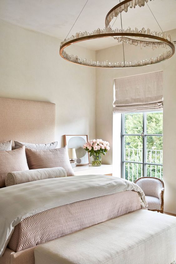 a soft and lovely bedroom with a pink upholstered bed, crystal chandeliers, pink and creamy bedding