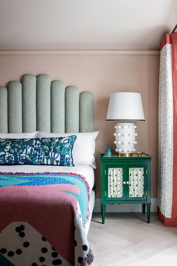 a pastel bedroom with a statement bed with a green statement headboard, bright bedding and textiles