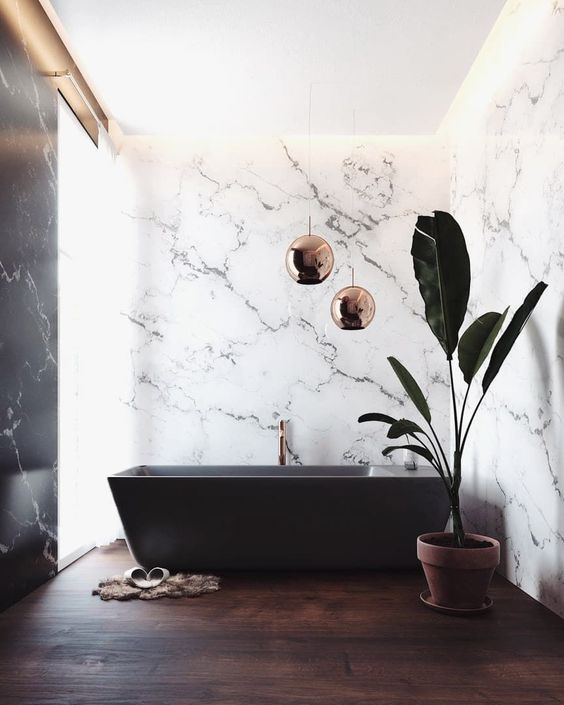46 a sophisticated bathroom with white marble walls, a dark stained floor and a black bathtub and copper lamps