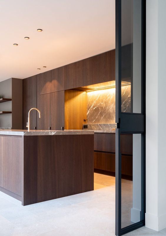 a minimalist walnut kitchen with sleek cabinetry, a grey marble backsplash and countertops and gold fixtures