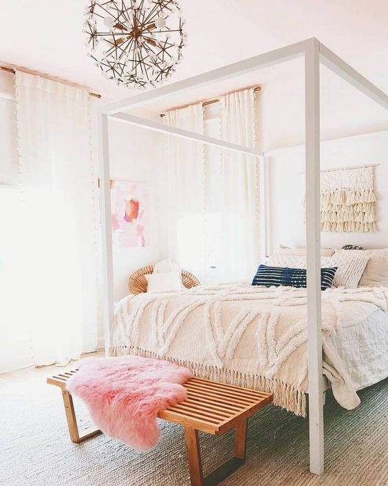 47 a neutral bedroom with a statement canopy bed, a bench with a pink throw, a lovely floral chandelier