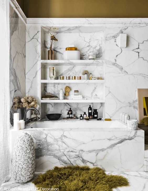 an eye-catchy modern bathroom with white marble, a niche with shelves, a bright rug and dried blooms