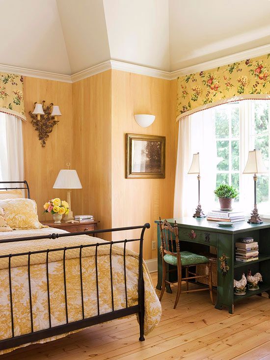 a country bedroom with yellow walls, a forged bed, yellow floral bedding and matching curtains plus a green desk
