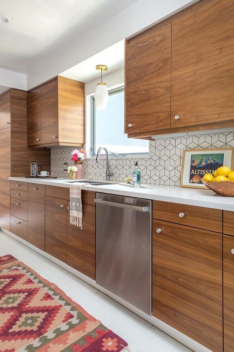 A mid century modern walnut kitchen with small knobs, white geometric tiles ont he backsplash and white countertops