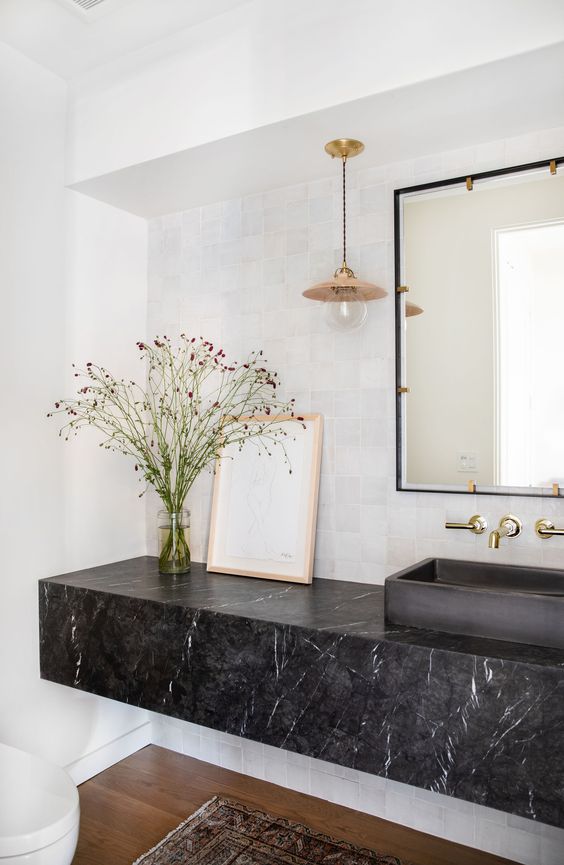 a modern bathroom with white walls, a black marble slab vanity and a black sink plus a large mirror
