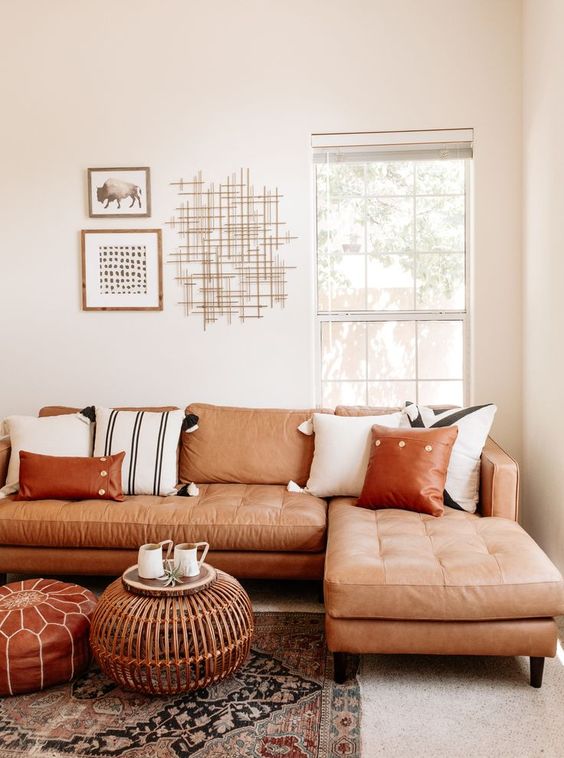 a neutral living room with a terracotta leather sectional, a leather and rattan ottoman and printed pillows