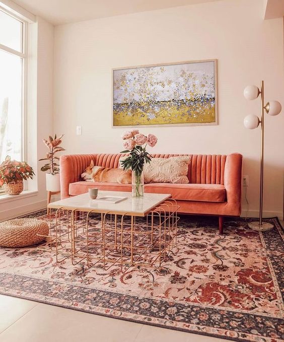 a cozy warm living room with a coral sofa, a printed rug, a copper table and a bold artwork