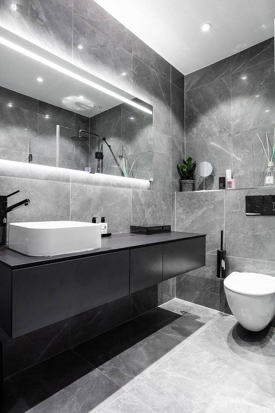 an elegant grey marble tile bathroom, a black floating vanity and a lit up mirror plus white appliances