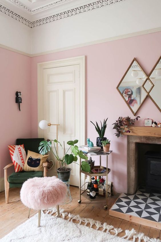 53 a cheerful pink living room with a green chair, a pink stool, a fireplace with tiles and potted plants