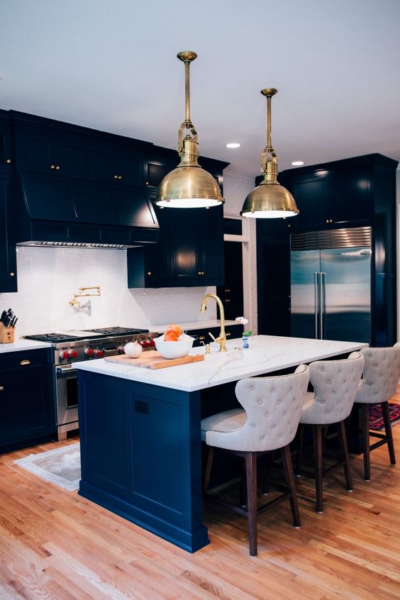 a stylish modern navy kitchen with a white stone backsplash and countertops, gold touches and pendant lamps