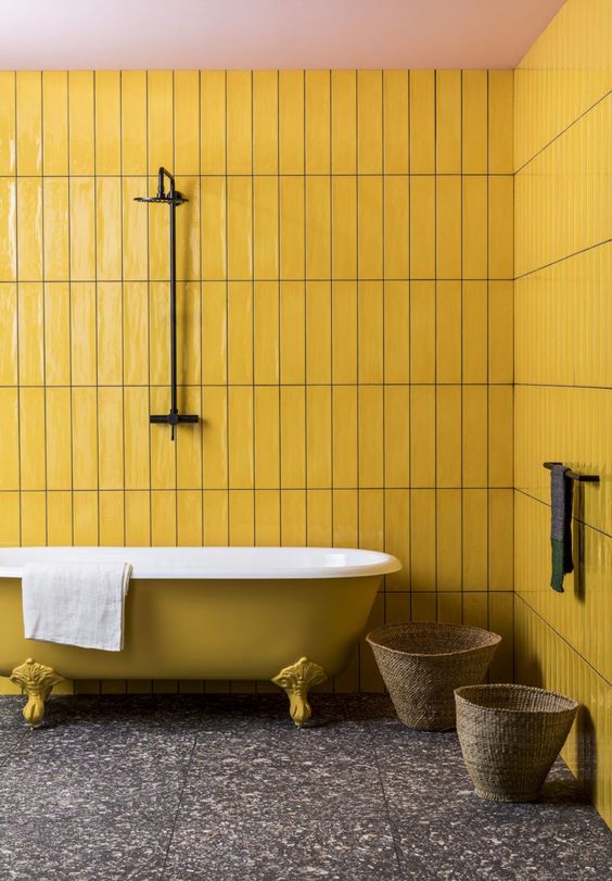 a bright yellow bathroom with skinny tiles, a clawfoot bathtub, a grey terrazzo floor is very catchy and bold