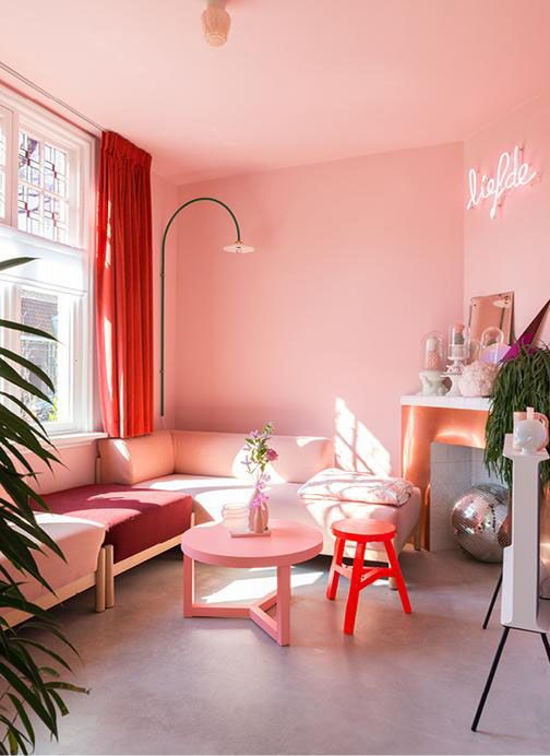 A bright and fun pink living room with a sectional, a non working fireplace, a neon sign and colorful furniture