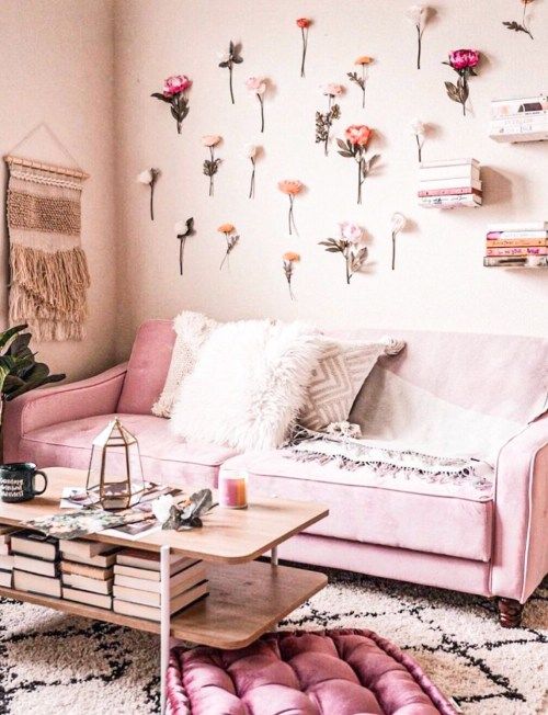 a pink living room with light pink walls, a bright pink sofa and an ottoman, flowers attached to the wall and a wooden table