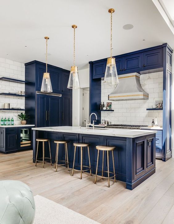 a beautiful navy kitchen with vintage cabinets, white marble countertops, a white tile backsplash and cool pendant lamps