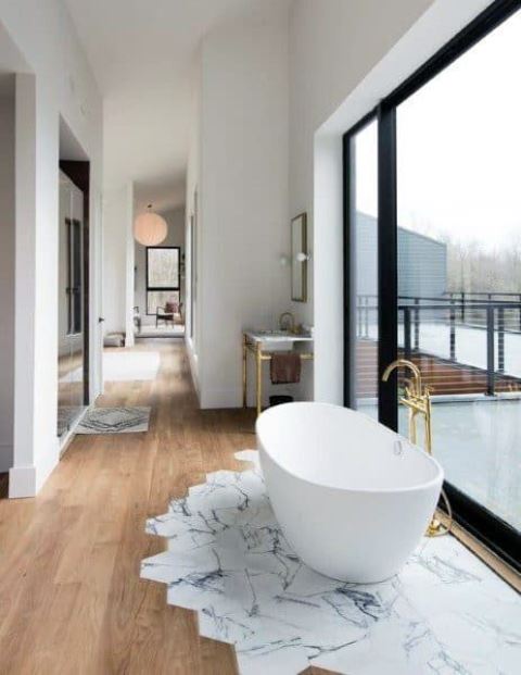 62 an airy bathroom with a glazed wall, a floor transition with marble and wood tiles and an oval bathtub