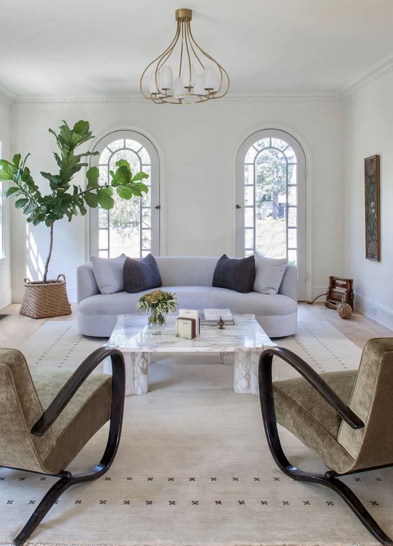 an airy and welcoming living room with a curved sofa and unique curved chairs, a statement plant and a modern chandelier