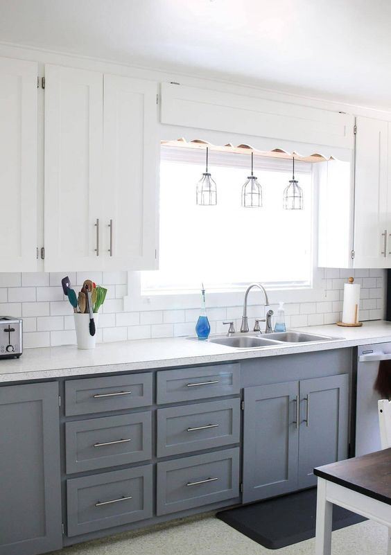 a modern two-tone farmhouse kitchen with white and grey cabinets, a white subway tile backsplash, white countertops and pendant lamps
