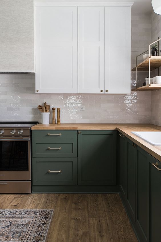 a laconic dark green and white kitchen, with glossy white marble tiles, a butcherblock countertop and simple fixtures