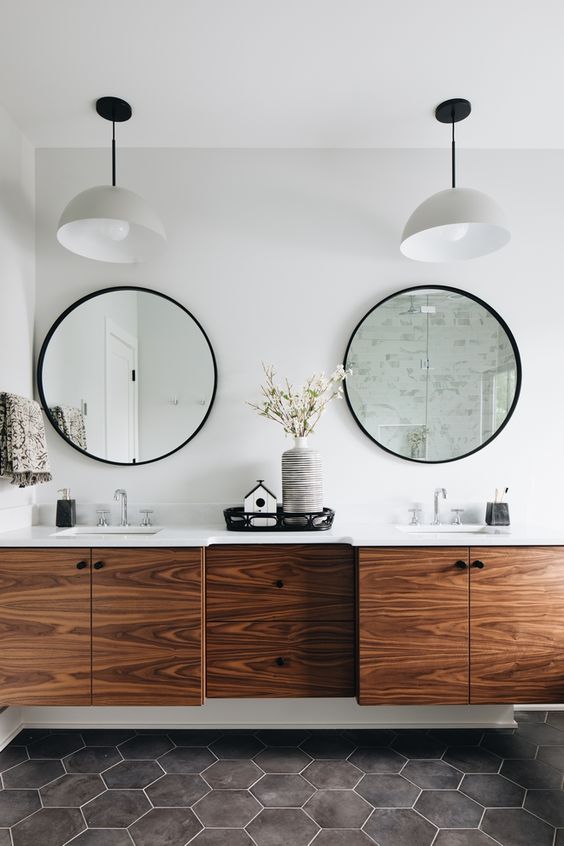 a modern bathroom with grey hex tiles on the floor, a rich-toned floating vanity and round mirrors