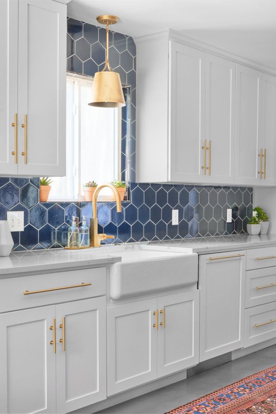 a chic white kitchen with a navy hex tile backsplash and white grout, gold fixtures and a pendant lamp is amazing