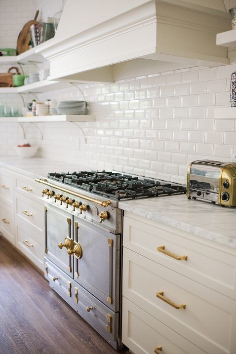 a beautiful vintage kitchen in white, with a white subway tile backsplash and gold fixtures for a more elegant feel