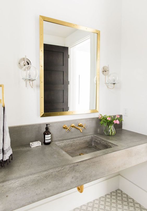A concrete floating vanity with a built in sink and gold fixtures that soften the look and make the bathroom cooler