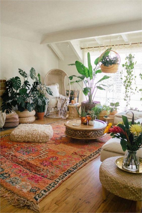 a boho living room with neutral furniture, a statement rug, lots of potted plants and woven ottomans